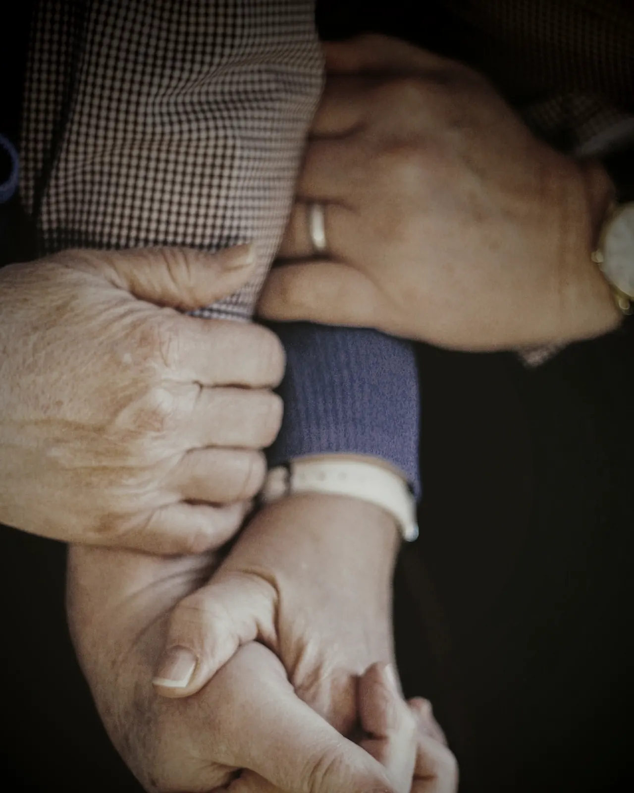 Mãos de uma pessoa idosa amparadas por outras duas pessoas, em close.